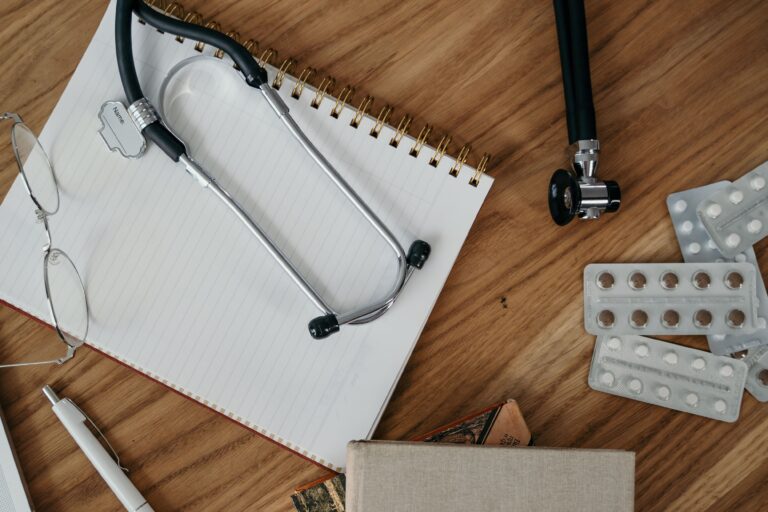 Estetoscopio y libreta sobre un escritorio junto a medicamentos, representando atención médica