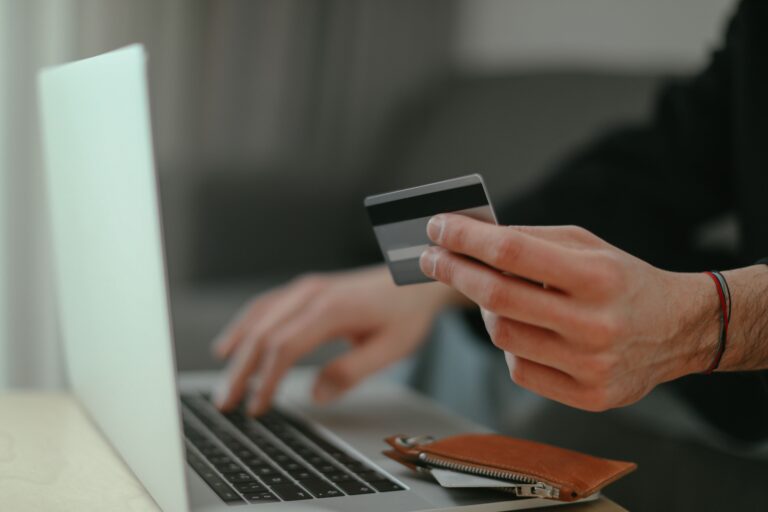 Persona sosteniendo una tarjeta de crédito frente a una laptop al hacer una compra en línea