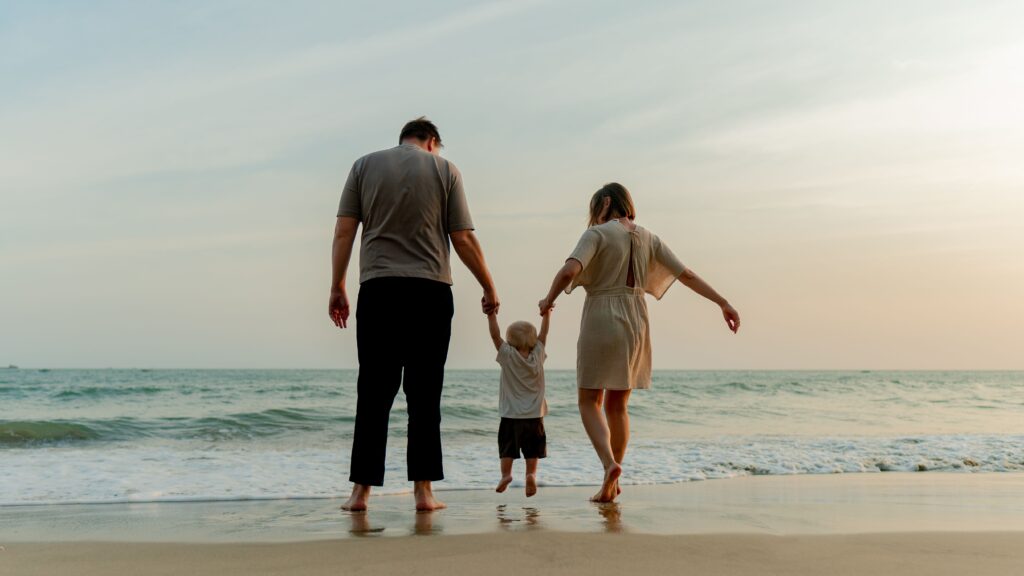 Familia caminando por la orilla del mar tomados de la mano al atardecer