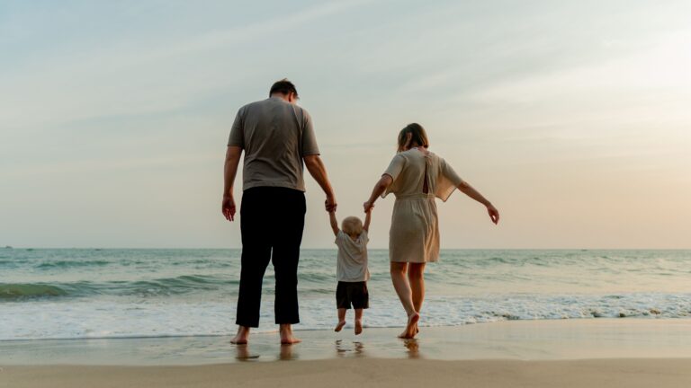 Familia caminando por la orilla del mar tomados de la mano al atardecer